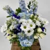 Blue hydrangeas, white daisies, and cream roses arranged in a clear glass vase.