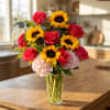 Tall vase of yellow sunflowers, pink roses, and pale hydrangeas on a wooden kitchen island