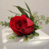 Single red rose boutonniere resting on a white surface