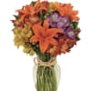 Lilies, alstroemeria and more in a rose glass vase tied with raffia.