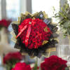 Round bouquet of tightly packed red roses wrapped in black and gold paper with red ribbons.