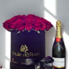 Black hat box of red roses beside a champagne bottle with scattered rose petals.