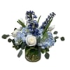 Blue hydrangeas, white roses, white tulips, and blue delphinium arranged in a clear glass cylinder vase