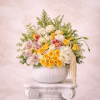 Yellow and white floral arrangement with roses, orchids, and tulips in a round white vase on a pedestal.