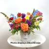 Bright mixed flower arrangement with orange roses, tulips, daffodils and other blooms in a white vase