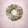 Standing round wreath of pink and white roses with a white bow on a wooden easel