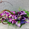 Long modern centerpiece of purple calla lilies and orchids with curved vine accents