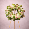 Standing wreath of white and pink flowers with green accents on a wooden easel.