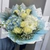 Bouquet of pale yellow roses, blue hydrangeas, and white flowers wrapped in blue paper
