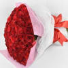 Large bouquet of red roses wrapped in pink paper and white mesh with a red satin bow