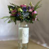 Colorful mixed bouquet with pink and blue flowers arranged in a tall glass bottle.