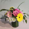 Mixed bouquet of pink roses, gerbera daisies, hydrangea, and yellow gerbera in a leaf-lined glass vase
