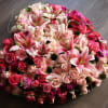 Heart-shaped arrangement of pink lilies, roses, and gerbera daisies in various pink and red tones