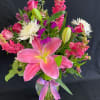 Tall mixed arrangement of pink lilies, roses, snapdragons and white mums in a clear vase with a ribbon bow