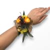 A rustic-chic wrist arrangement featuring warm orange and yellow roses, dramatic blue
