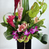 Tall tropical arrangement with pink lilies, orchids, ginger flowers, and sculpted green leaves in a black vase