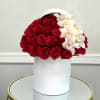 Red roses and white orchids arranged in a white hatbox-style cylinder container on a mirrored table