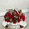 Round basket of red roses with eucalyptus in a white woven handle basket on a mirrored table