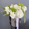 White and green flower arrangement with roses and hydrangeas in a tall silver hatbox-style container