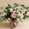 Round vase arrangement of peach roses and white alstroemeria with a pink ribbon bow.