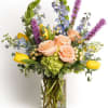 Mixed bouquet of peach roses, yellow tulips, purple and blue blooms in a clear glass vase