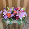 Low arrangement of pink lilies, orange roses, and purple mums in a rustic wooden box
