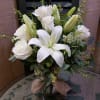 Arrangement of white lilies and roses in a clear glass vase with a burlap bow.