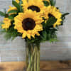 Tall glass vase of large yellow sunflowers with dark centers
