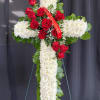 Tall white chrysanthemum cross with red roses and a red memorial ribbon on a metal easel.