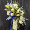 Standing spray of white mums, yellow roses, lilies, and blue flowers with blue ribbon on an easel.