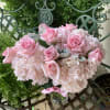Low glass vase of light pink roses and hydrangeas arranged in a compact mound on a metal bench