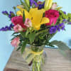 Bouquet of yellow lilies, pink roses, and purple filler flowers in a glass vase
