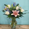 Pink lily and white roses in a glass vase with blue flowers