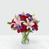 Bouquet of red roses, pink lilies, and purple blooms in a glass vase