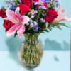 Bouquet of pink lilies, red roses, and purple daisies in a glass vase