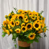 Large arrangement of yellow sunflowers in a tall clear glass vase on a table
