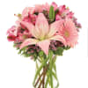 Pink lilies, gerbera daisies, and mixed blooms arranged in a clear glass vase