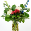 Red, white, and blue mixed flower arrangement with lush foliage in a clear glass jar vase