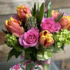 Bright bouquet of pink roses, orange-yellow tulips, and green hydrangeas in a glass vase with a floral bow