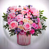 Pink and cream rose arrangement with lavender filler flowers in a pink glass vase