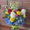 Bright mixed bouquet with blue hydrangeas, yellow daffodils, tulips, and white flowers in a clear glass vase