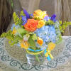 Colorful bouquet of yellow and orange roses, blue hydrangeas, orchids, and irises in a clear glass vase.