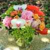 Mixed bouquet of pink carnations, roses, orchids, and orange blooms in a clear glass vase