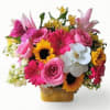 Bright mixed bouquet of pink roses, gerbera daisies, sunflowers, and white orchids in a basket with a pink butterfly.
