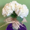 White hydrangea bouquet wrapped in burlap and tied with raffia in a glass vase