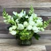 White roses and snapdragons with green accents arranged in a clear glass cube vase
