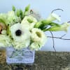 Low rectangular arrangement of white blooms with calla lilies in a glass vase wrapped in lace