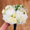 Hand-tied bouquet of white hydrangeas, roses, carnations, and alstroemeria with a dark ribbon-wrapped handle.