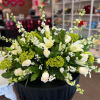 Large white and green arrangement with roses, lilies, and hydrangeas on a black-draped stand