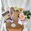 Gift caddy with pastel mixed flowers and a box of chocolates on a wood slice base.